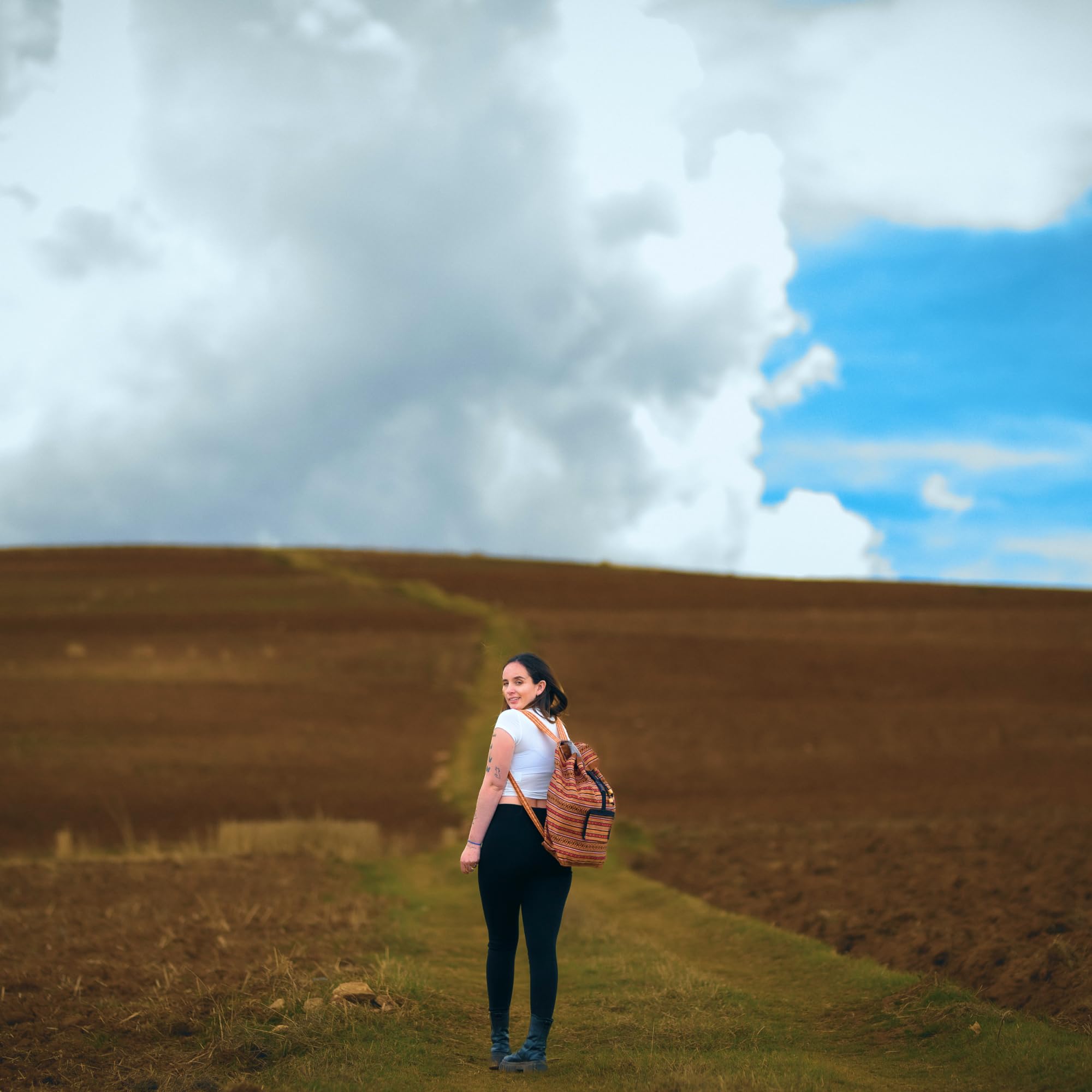 Woman with a backpack standing in a field with a blue sky and clouds.