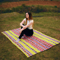 Woman sitting on a colorful striped blanket in a grassy field