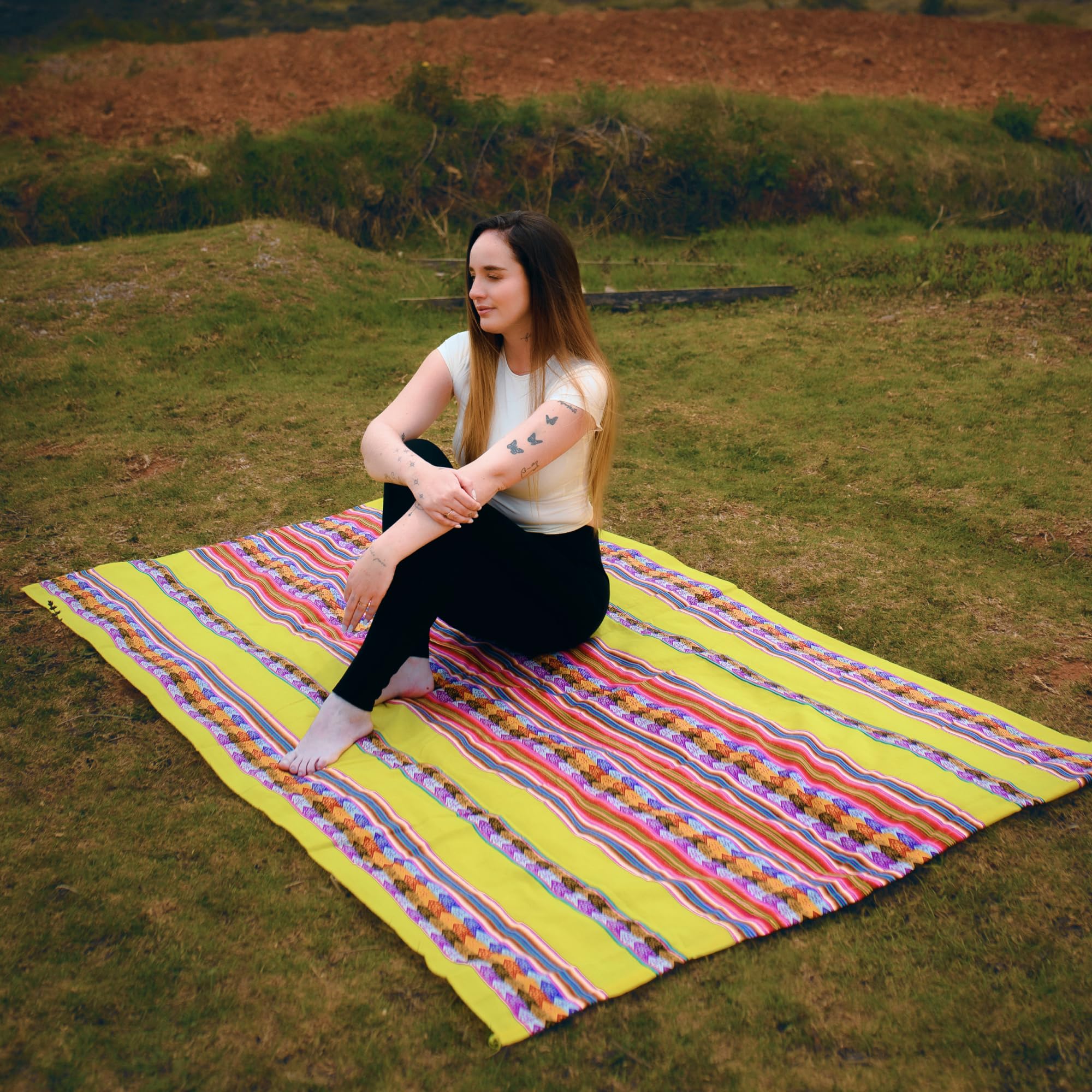 Woman sitting on a colorful striped blanket in a grassy field