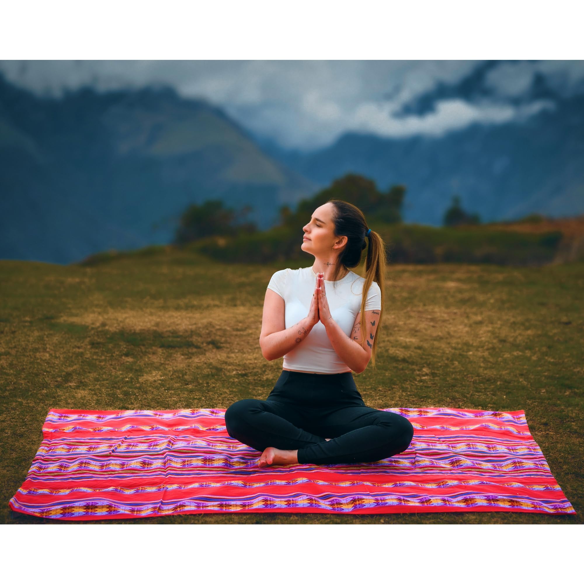 Woman meditating on a colorful mat with mountains in the background