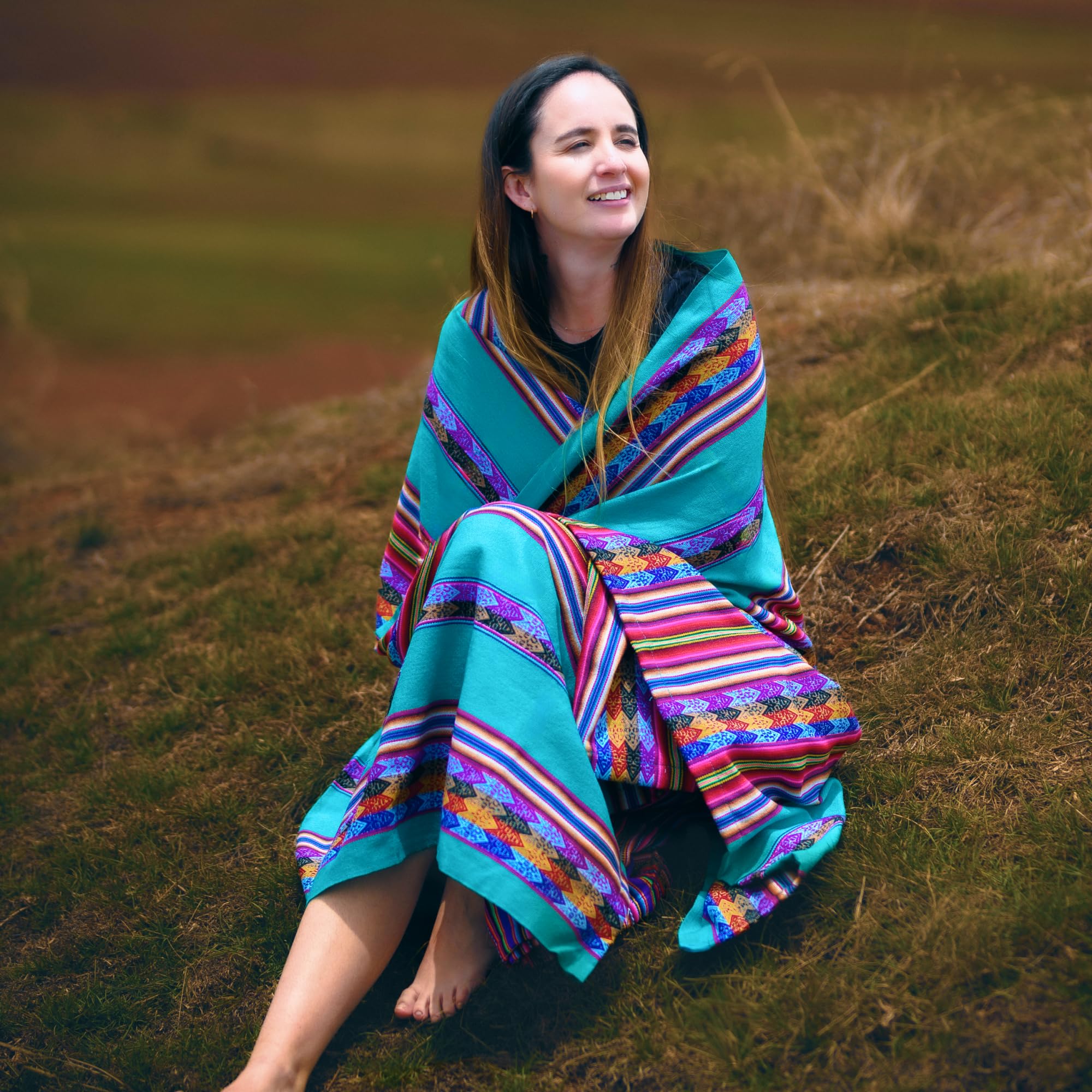 Woman sitting on a grassy field wearing a colorful blanket