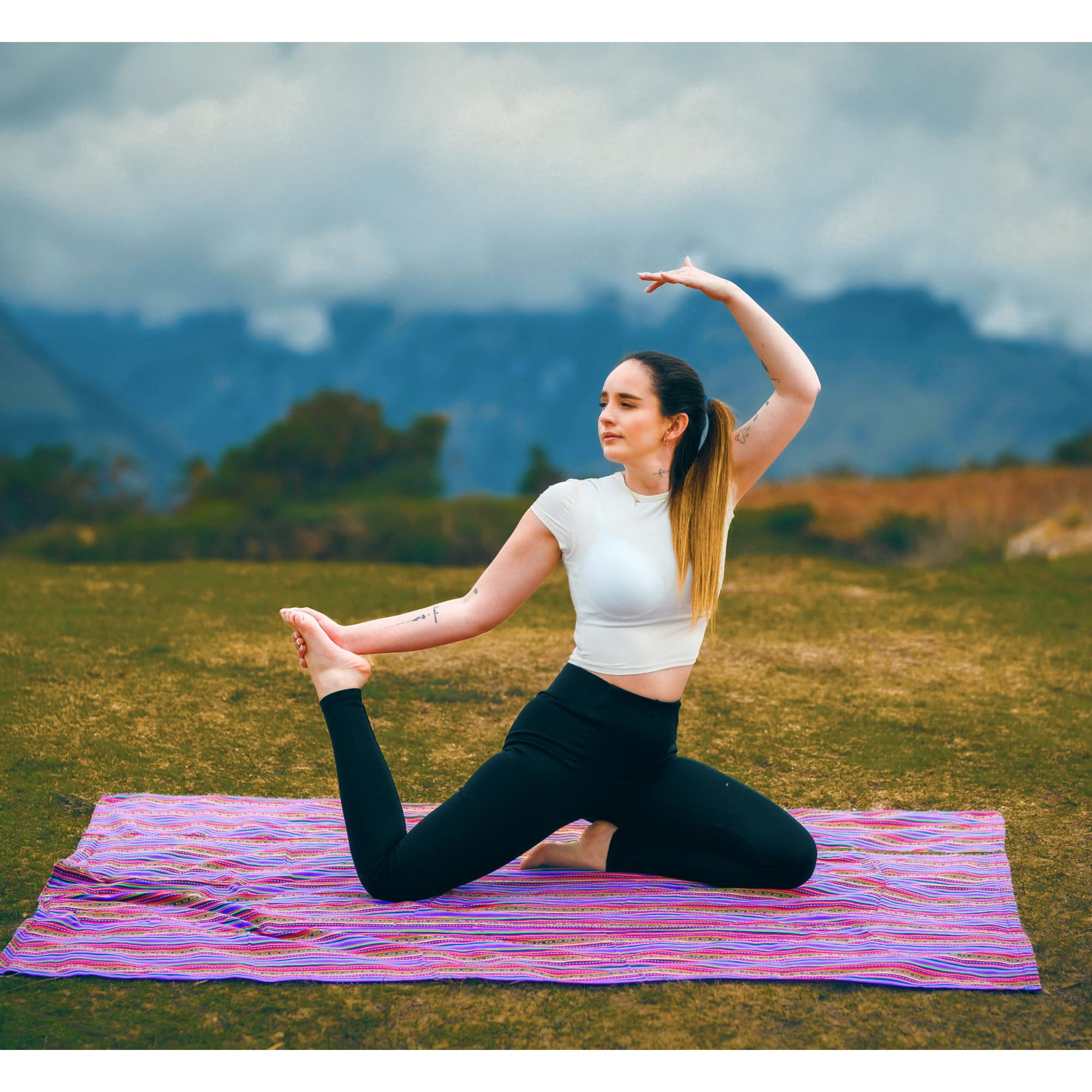 Woman practicing yoga on a colorful mat with mountains in the background