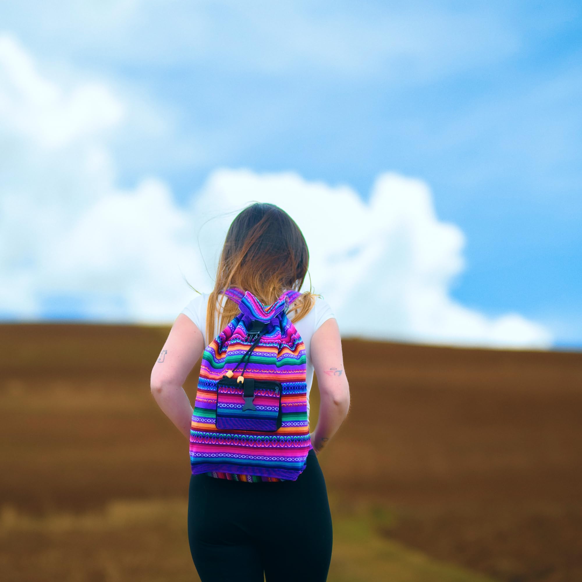 Person wearing a colorful striped backpack against a blue sky with white clouds.