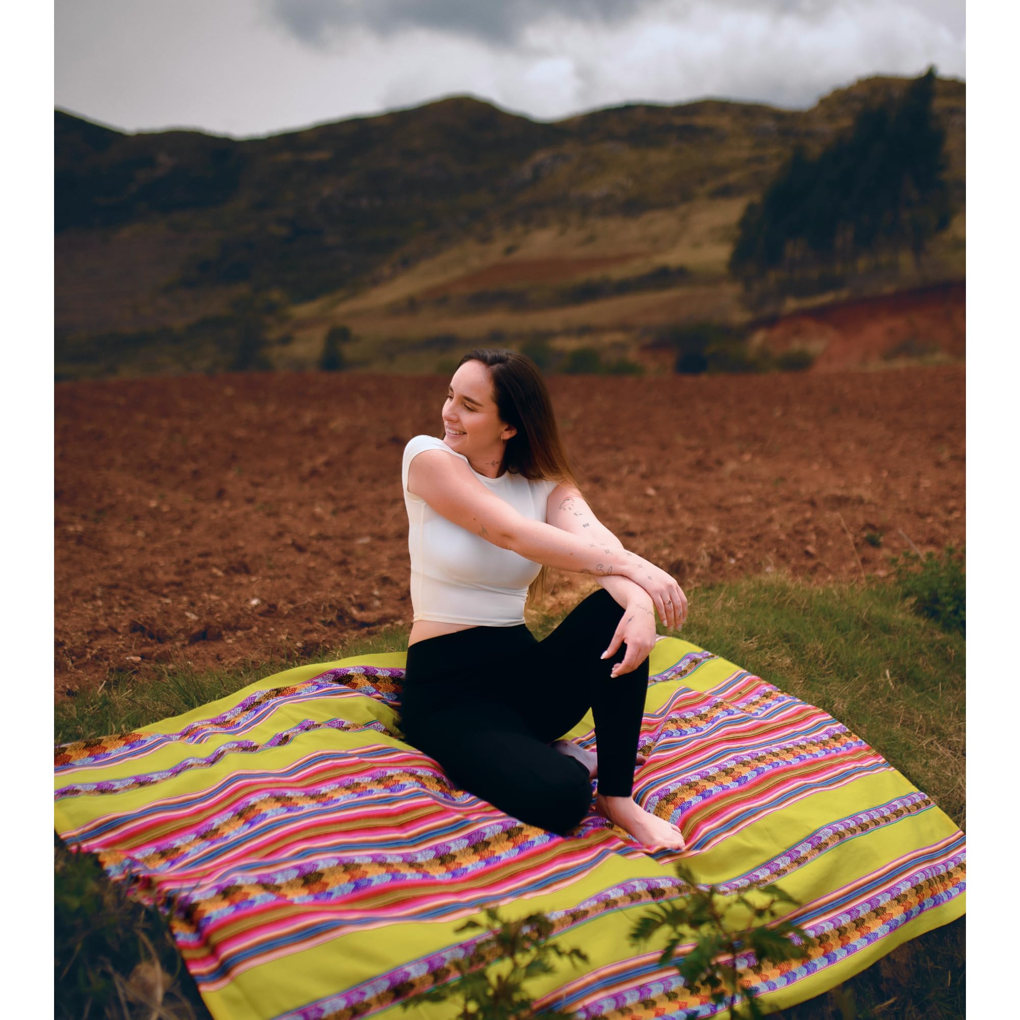 Woman sitting on a colorful blanket in a scenic outdoor setting with mountains.