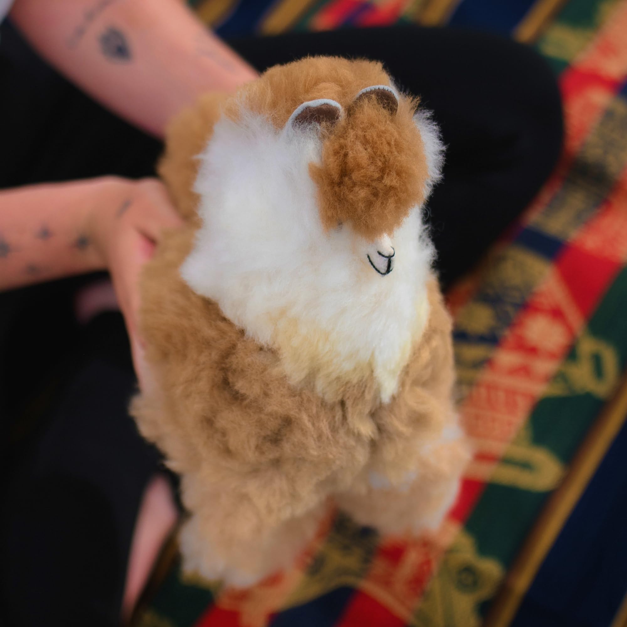Plush toy resembling a llama held by a person on a colorful patterned surface