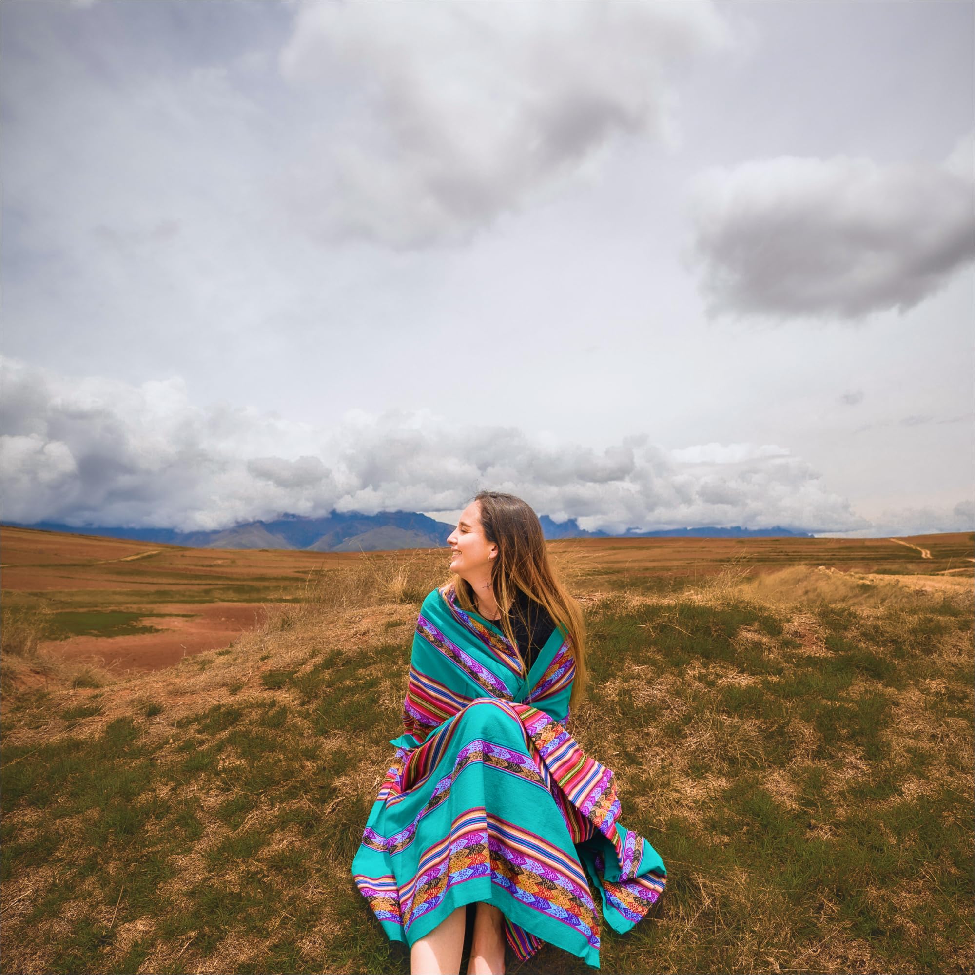 Woman in a colorful poncho standing in a vast, open field with mountains in the background