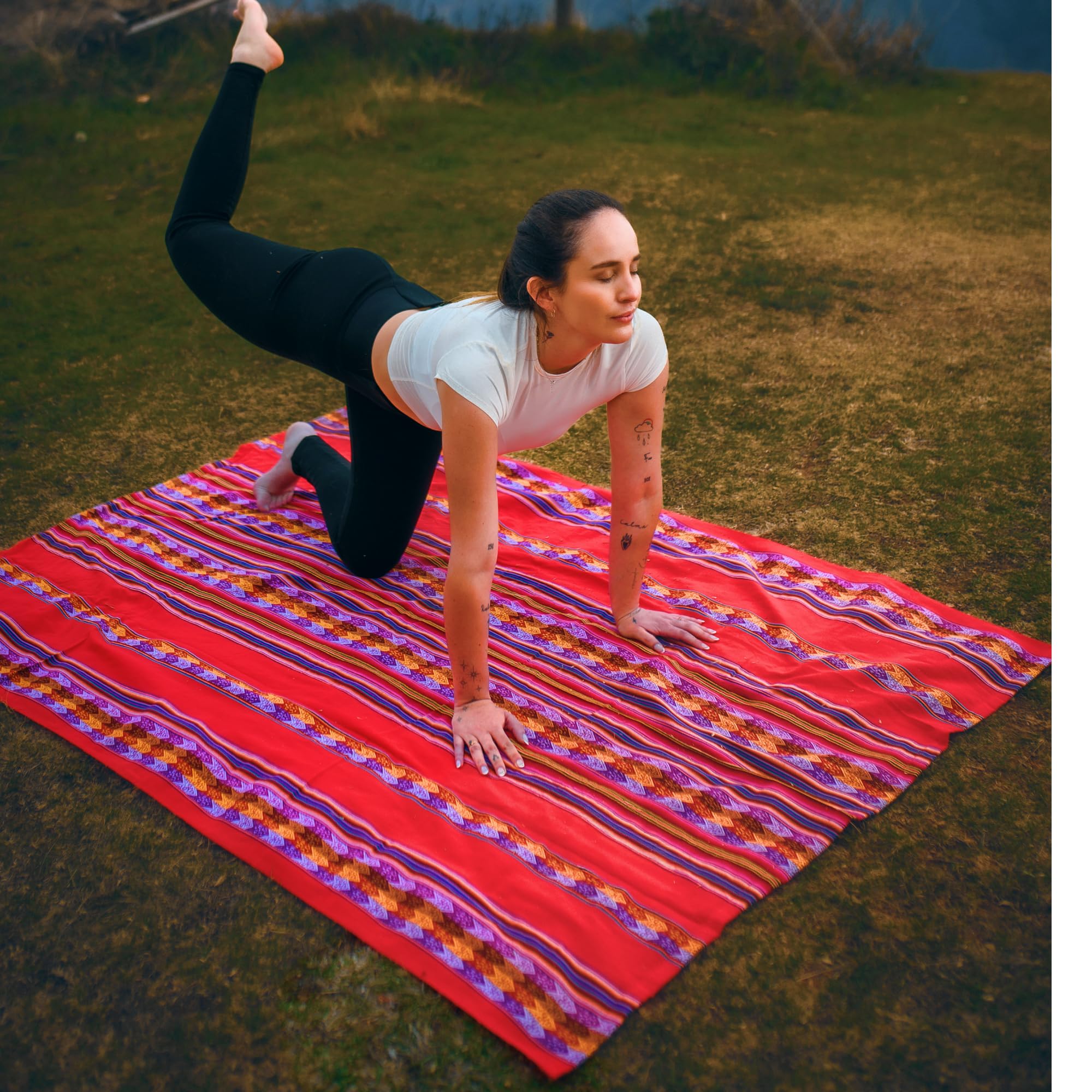 Woman practicing yoga on a colorful striped blanket in a grassy field