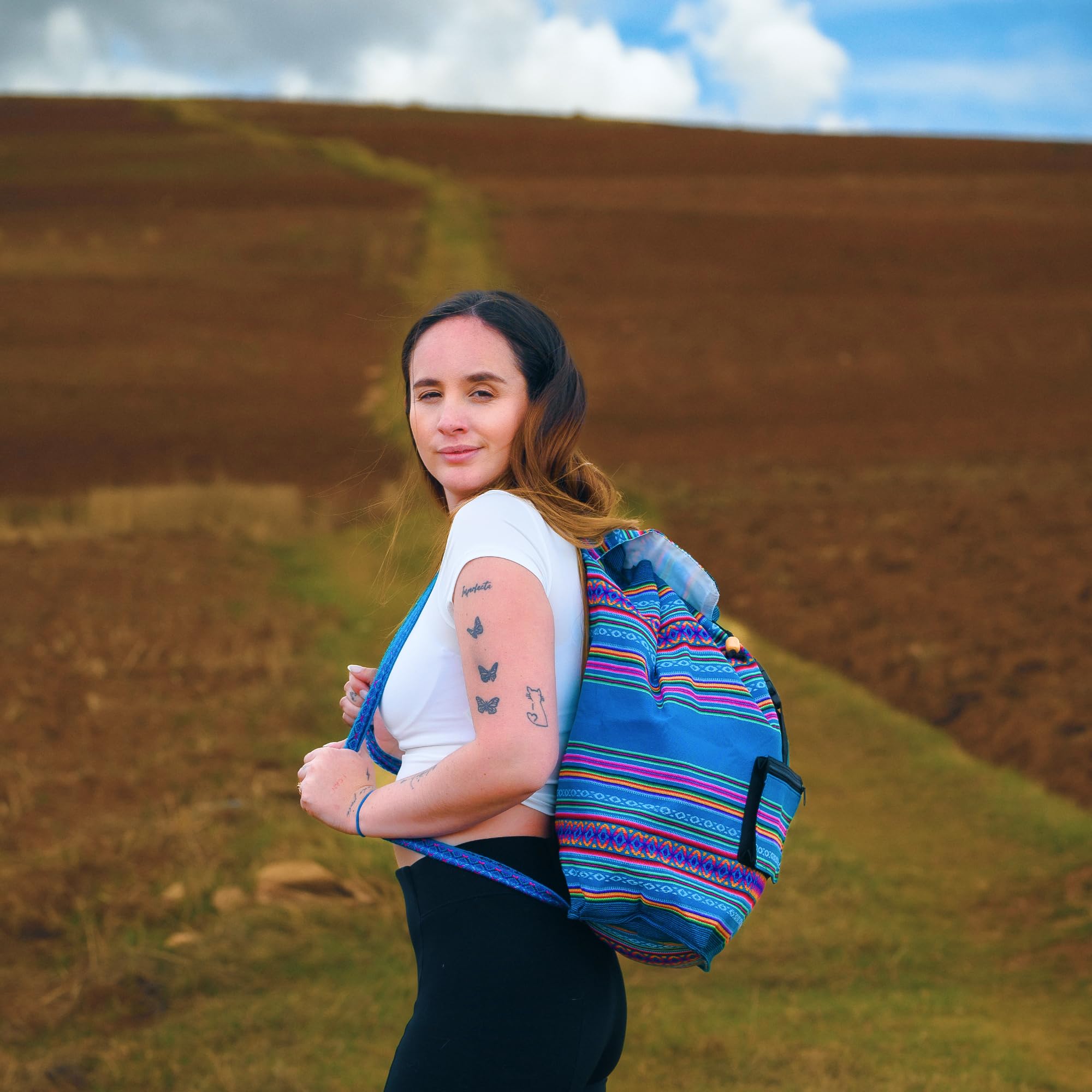 Woman with a colorful backpack standing in a field with a blue sky.