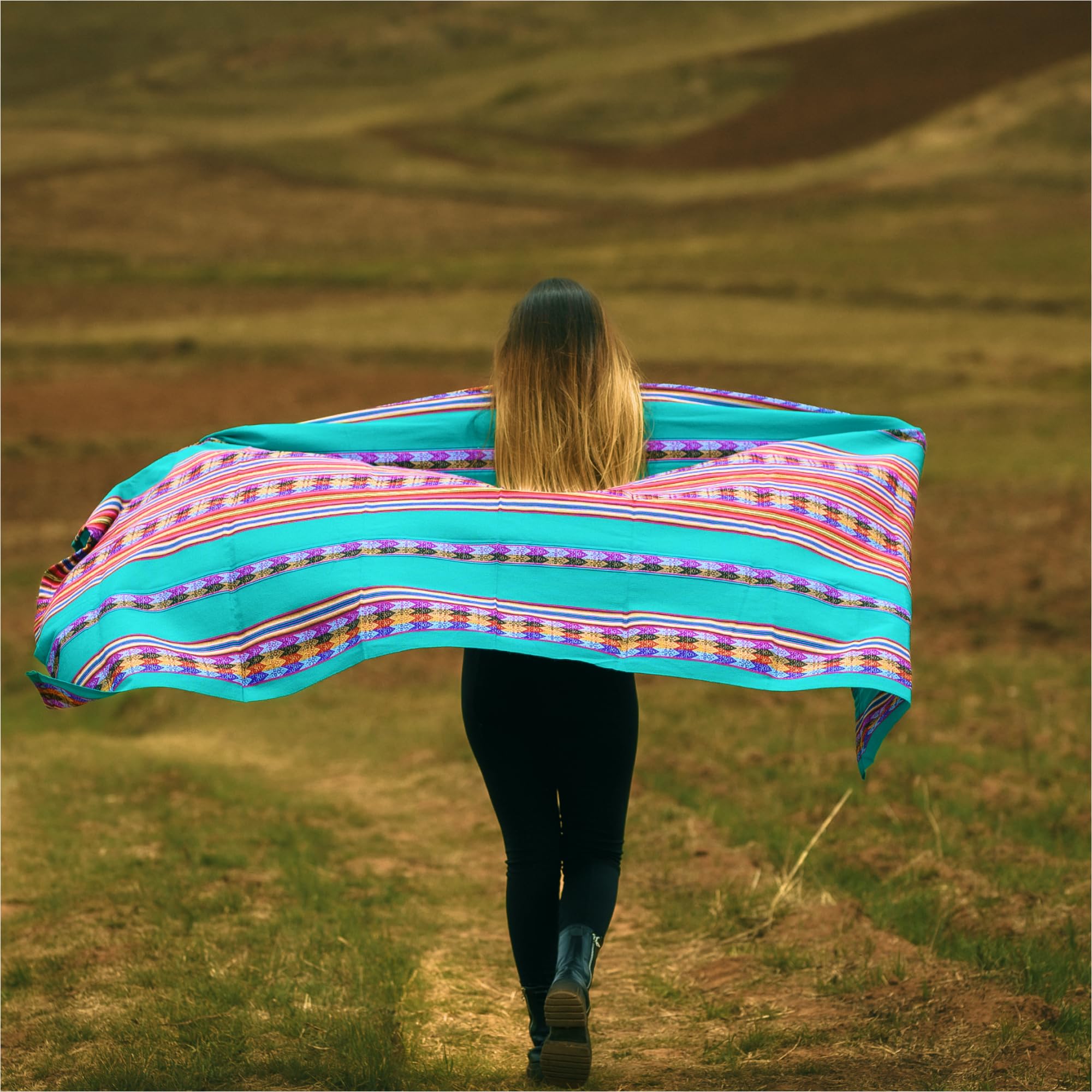 Person walking with a colorful striped blanket in a field