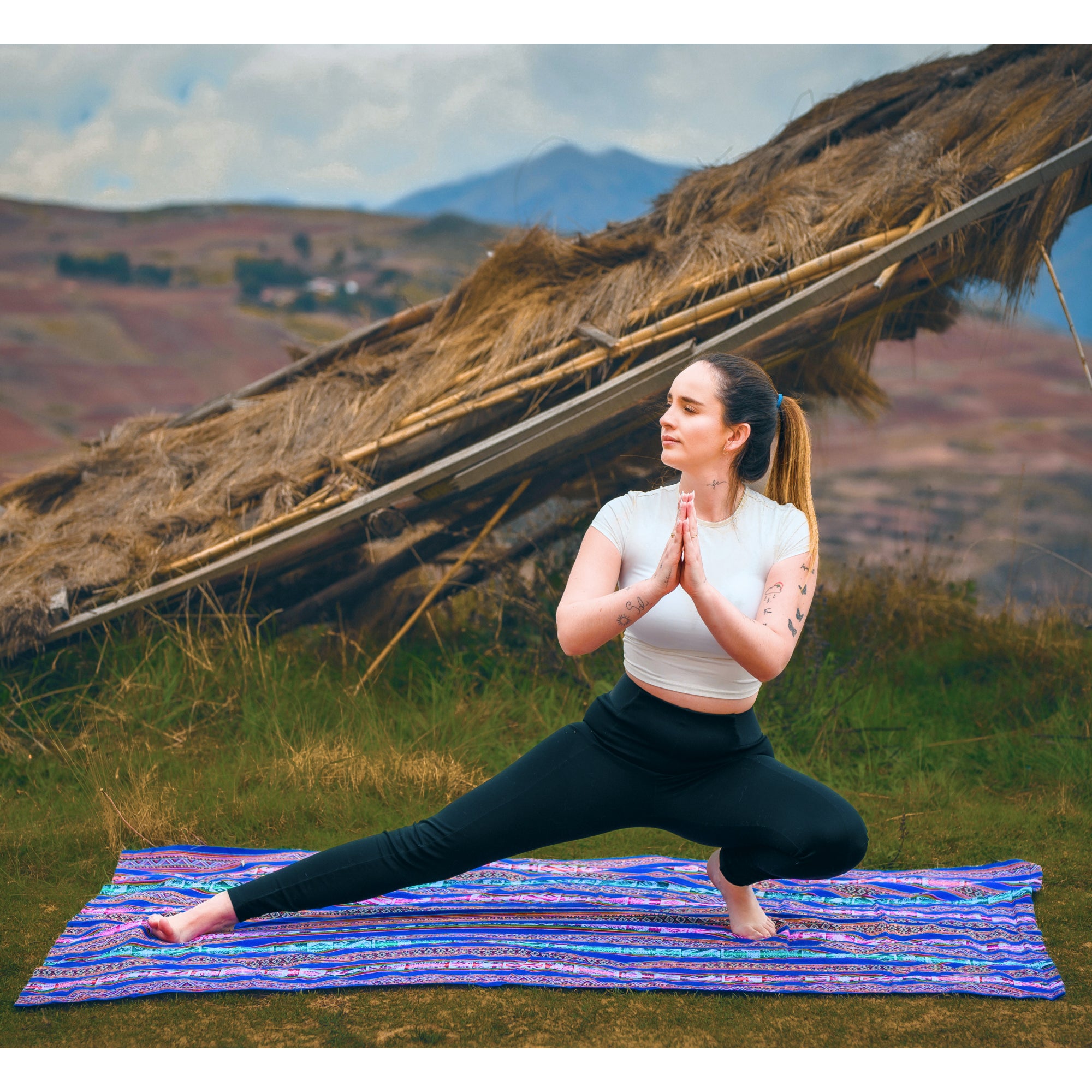 Woman practicing yoga on a mat with a scenic background of mountains and traditional architecture.
