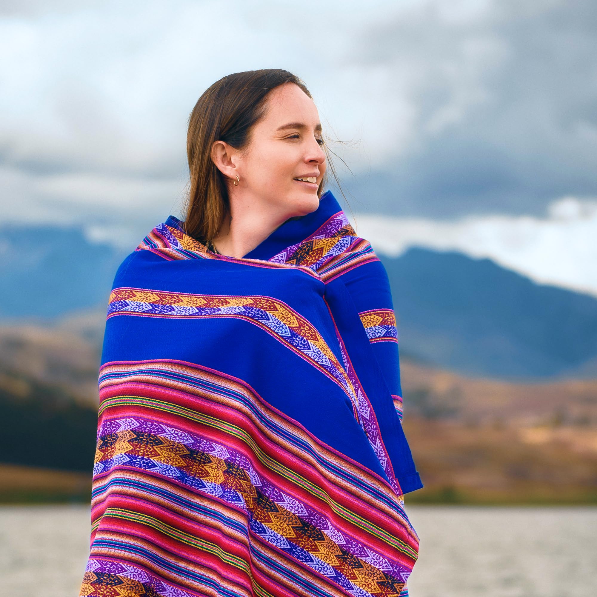 Woman wrapped in a colorful patterned blanket with mountains in the background