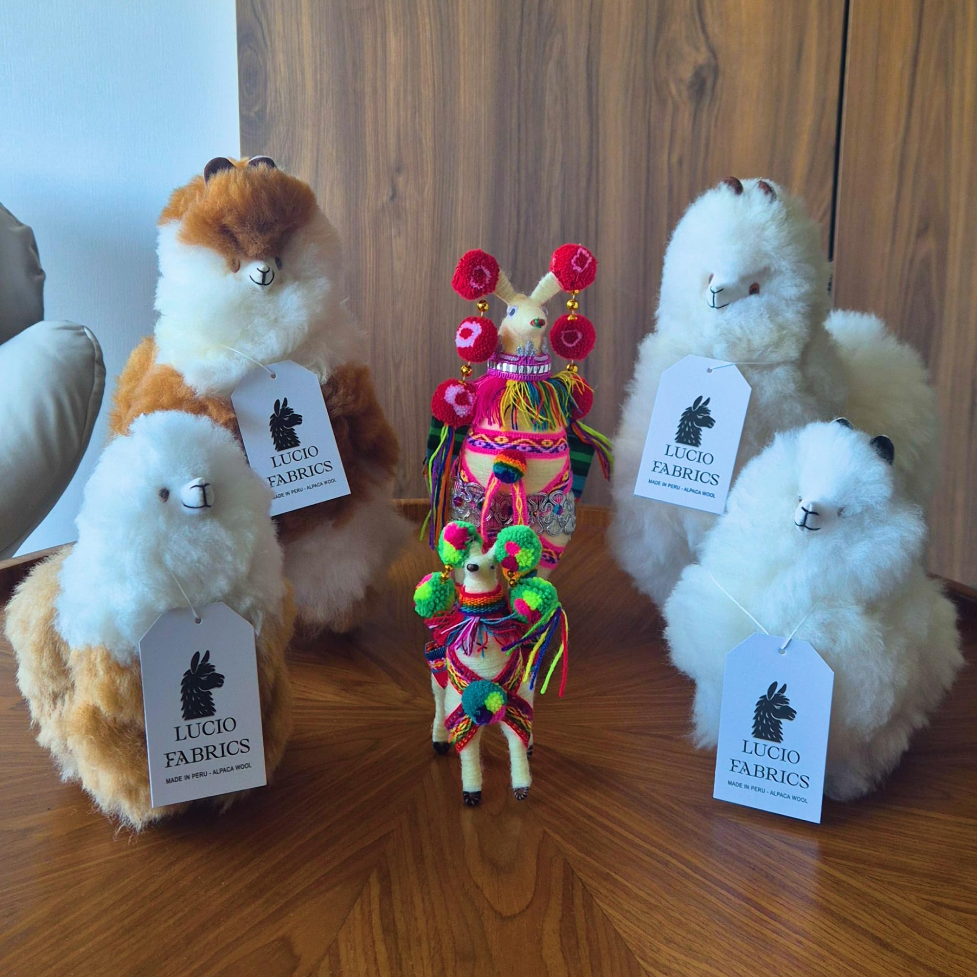 Plush toy llamas with colorful decorations on a wooden surface, featuring Lucio Fabrics tags.
