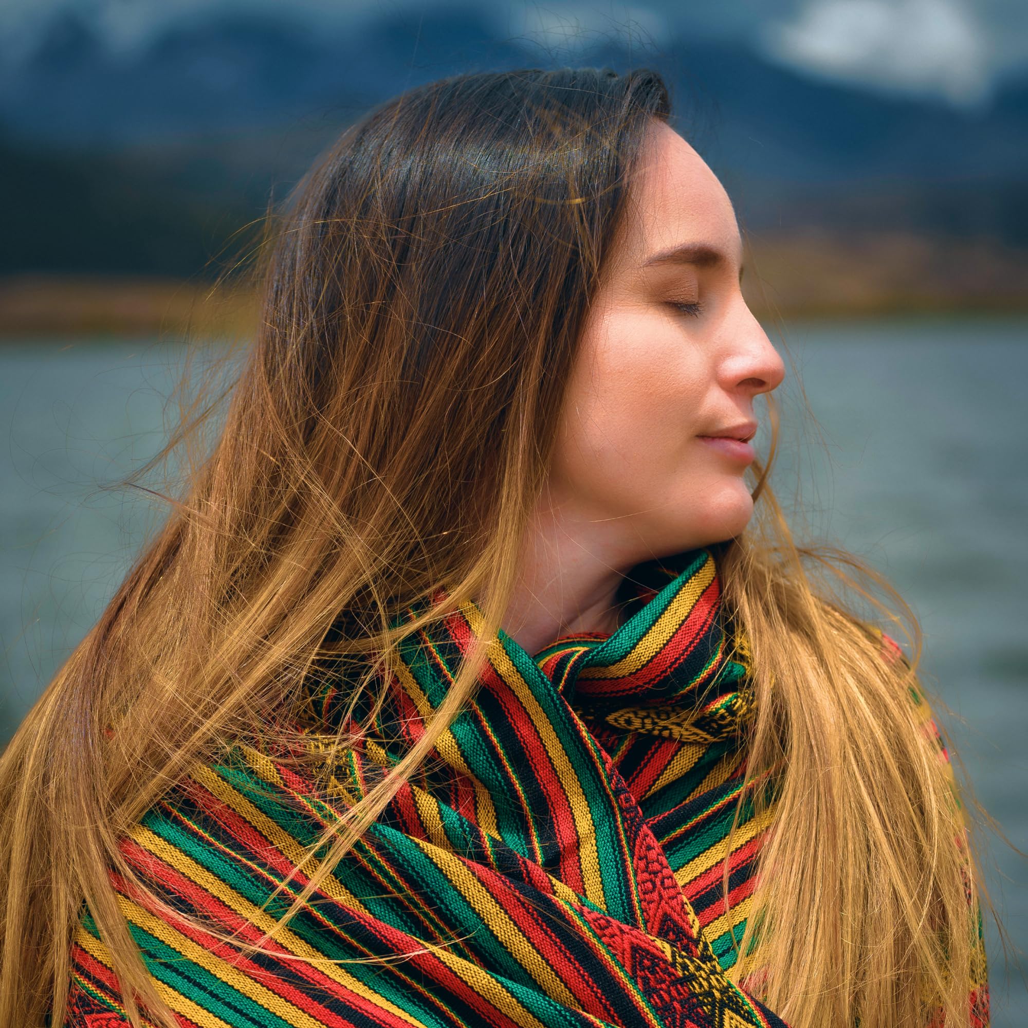 Woman with a colorful scarf standing by a body of water with mountains in the background