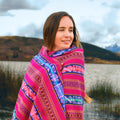 Woman wearing a colorful patterned shawl in a scenic outdoor setting with mountains and water.