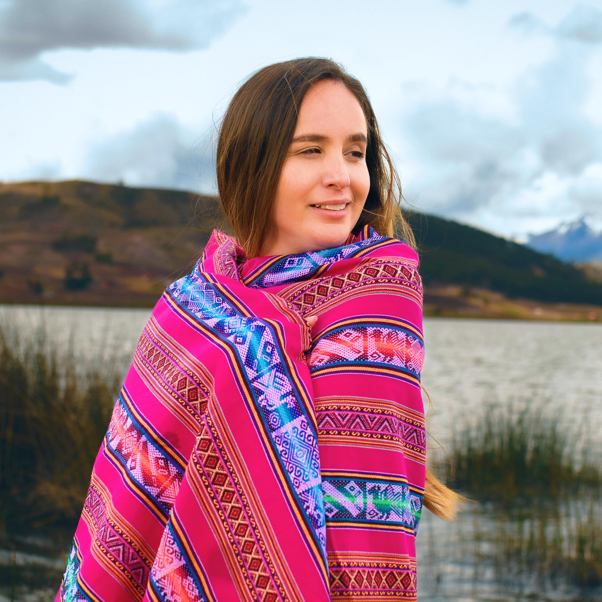 Woman wearing a colorful patterned shawl in a scenic outdoor setting with mountains and water.